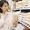 ドンキホーテの米売り場で、米袋を手に取り価格や内容を確認する日本人女性