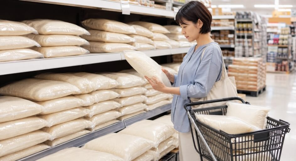スーパーの米売り場でパールライスのお米のような国産ブレンド米を比較して選ぶ日本人女性