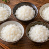 木製テーブルに並べた5つの茶碗の白ご飯を比較するイメージ