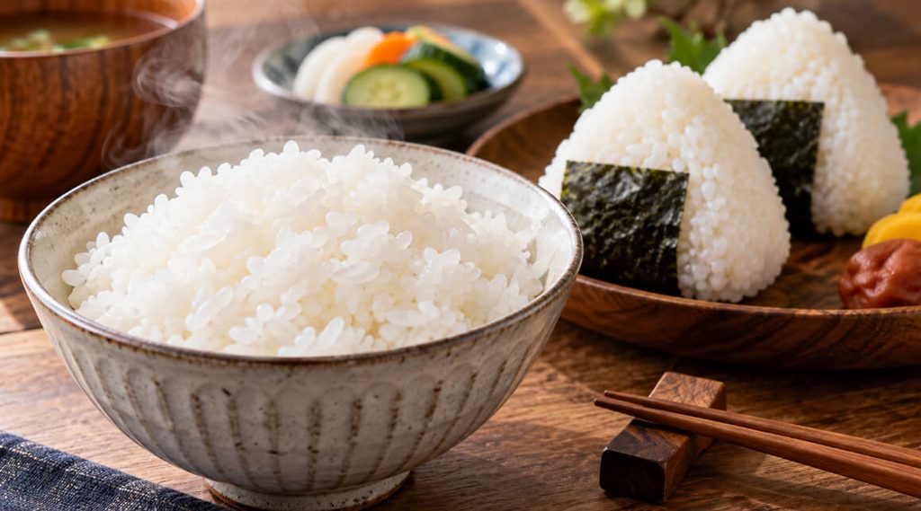 湯気の立つ炊きたての白ご飯と、海苔を巻いたおにぎりを並べた和食の食卓