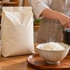 キッチンに置かれた米袋と計量カップの白米、炊飯器からよそった炊きたてご飯