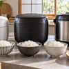 白・黒・シルバーの3種類の炊飯器と、手前に並べた白ご飯の茶碗