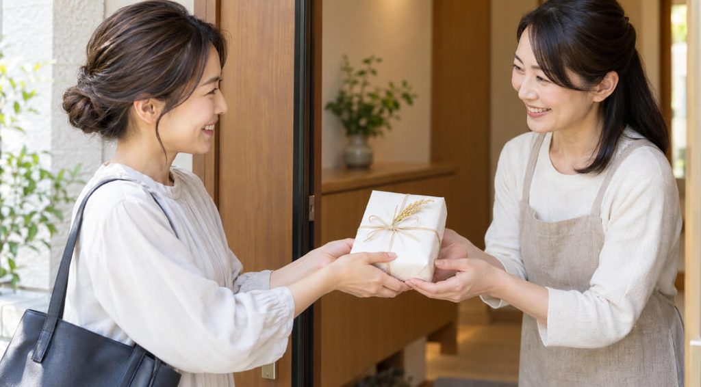 玄関先でお礼の品として小さな米ギフトを笑顔で手渡す日本人女性
